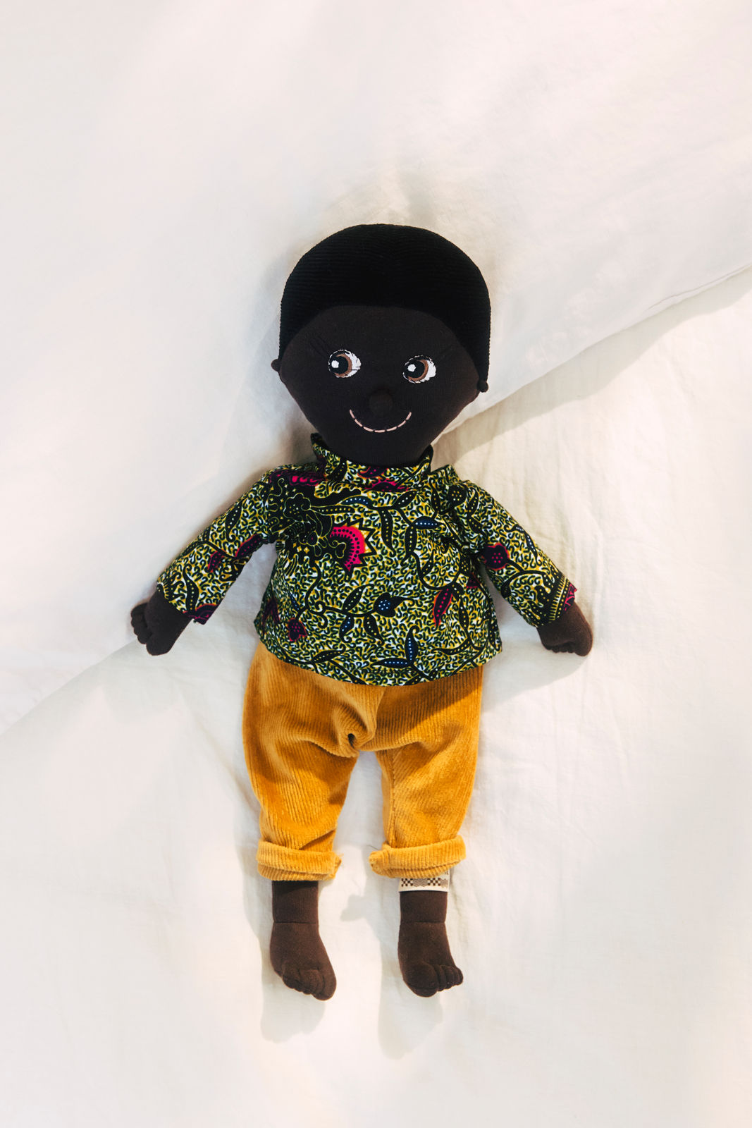 Kinderpuppe aus weichem Bio-Stoff, braun mit schwarzen Haaren und cord Hose.