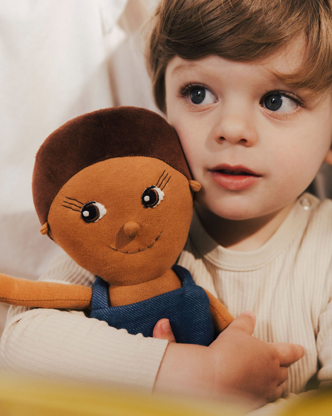 Lächelnde Stoffpuppe mit Latzhose, geeignet für Kinder ab 0 Jahre.