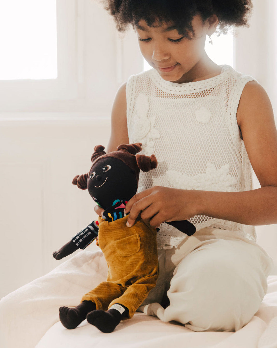 Kind zieht Kinderpuppe an. Kinderpuppe mit Latzhose