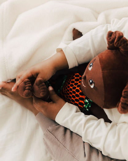 Kinderpuppe mit Haarzöpfen und Puppen Outfit aus Baumwolle. Kind hält Puppe im Arm