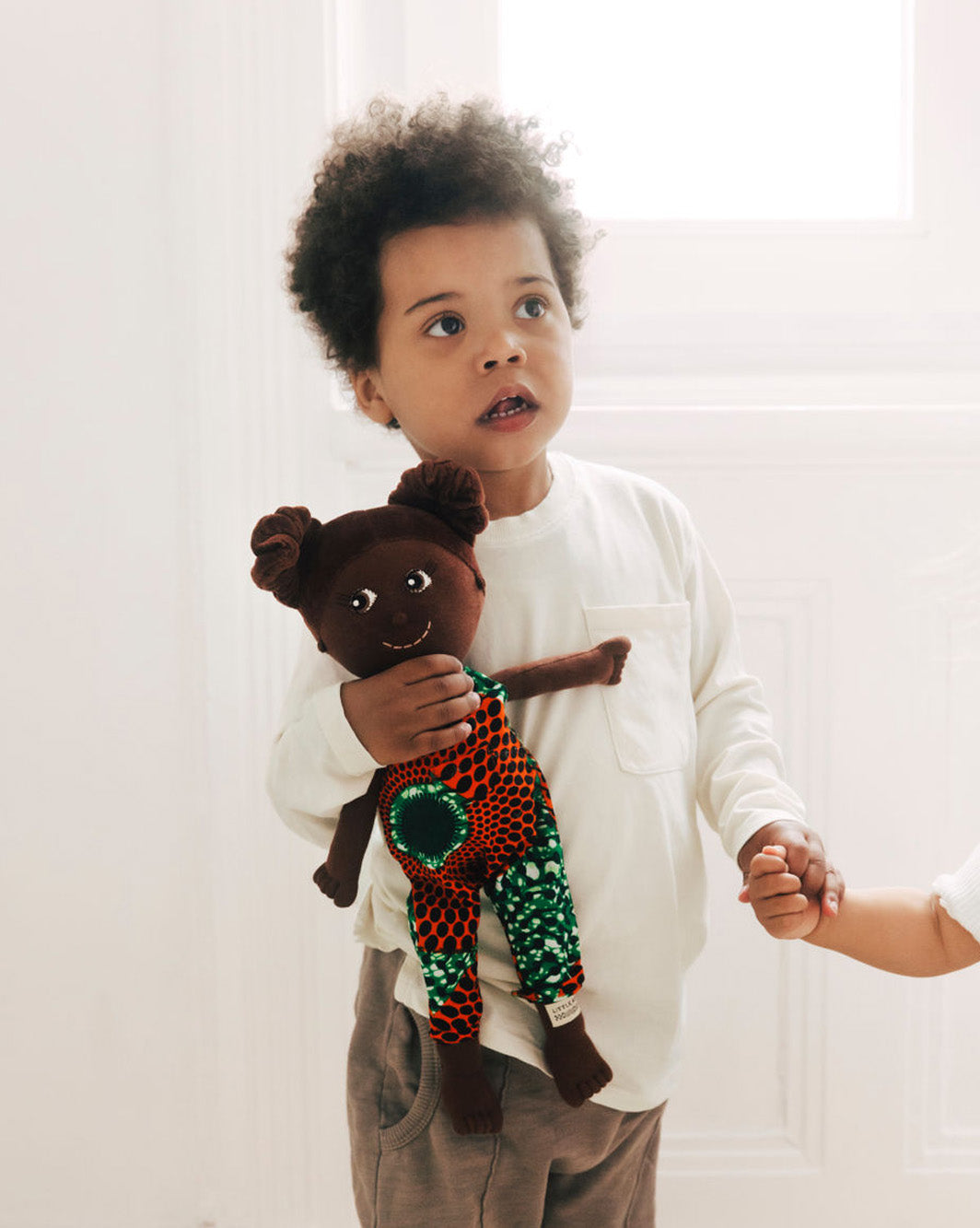 Kinderpuppe mit Haarzöpfen und Puppen Outfit aus Baumwolle. Kind hält Puppe in der Hand